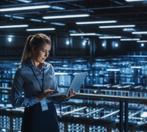 Data Center Female It Specialist Using Laptop. Server-Farm Cloud Computing und Cyber-Sicherheit Wartung Administrator arbeitet am Computer. Fachmann für Informationstechnologie.